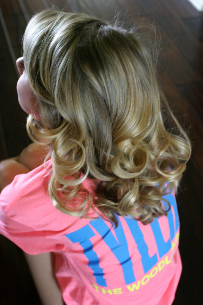 Girl in a pink and blue t-shirt with long blonde hair styled into voluminous curls.