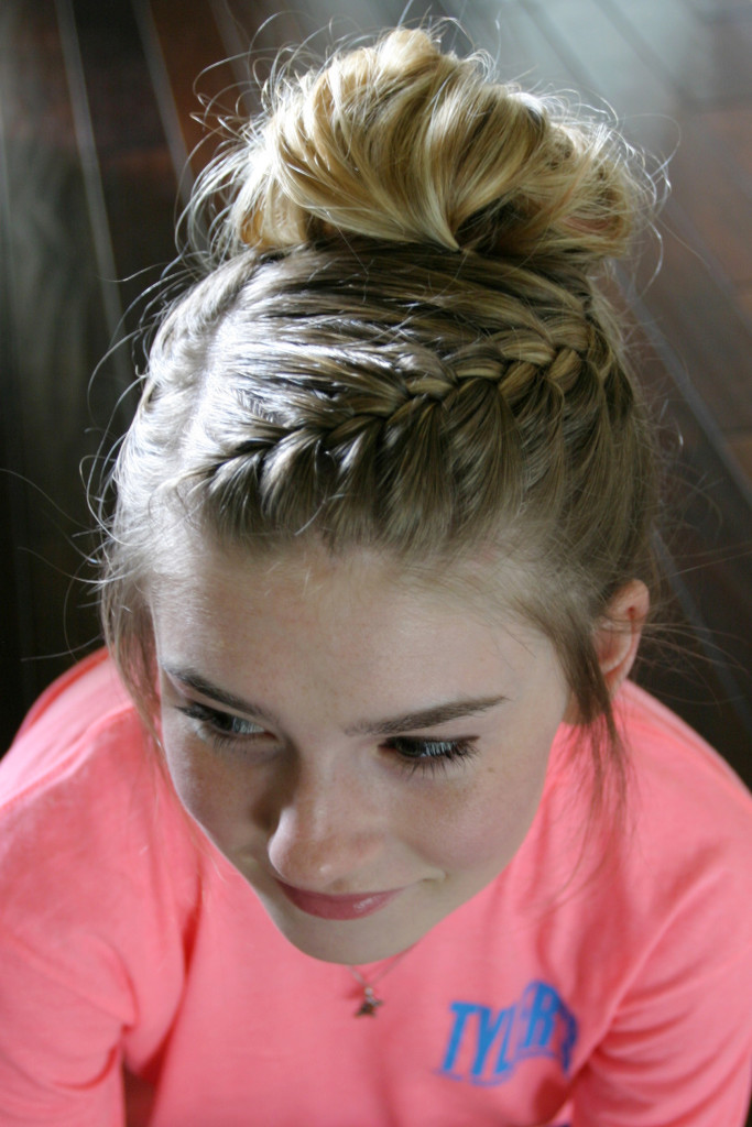 Front angle of a girl with an intricate side braid that ends in a blonde messy bun piled atop her head. 