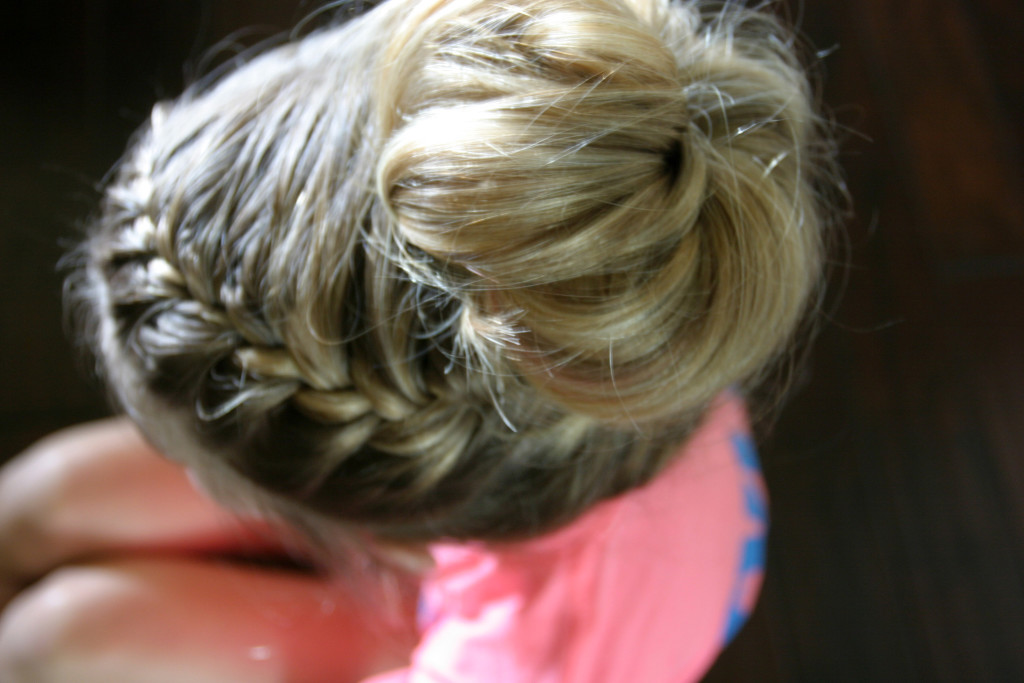 Looking down from above at the top of a girl's head with an intricate braid and blonde messy bun.