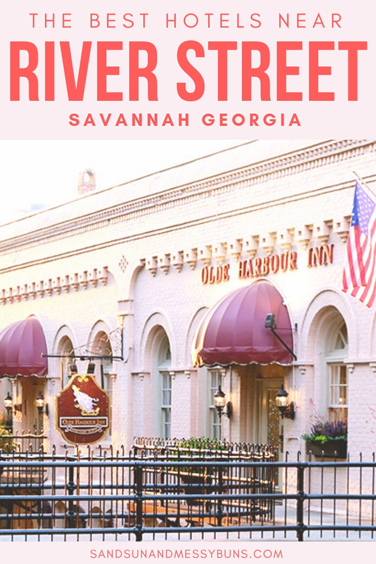 Exterior entry to the Olde Harbour Inn with pink-tinged painted brick walls and an American flag. Text overlay reads The Best Hotels Near River Street in Savannah Georgia.