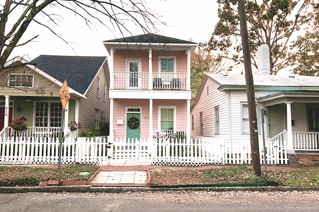 Cute two-story pink house with white trim, a green door, and a white picket fence in the yard. 