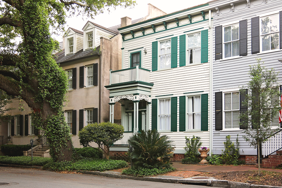 A row of 2-story colonial-style homes ranging in paint colors from brown to white with green shutters to blue with grey shutters. 