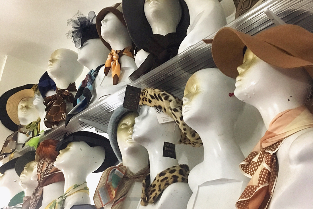 Rows of mannequin heads with funky vintage hats, scarves and sunglasses.