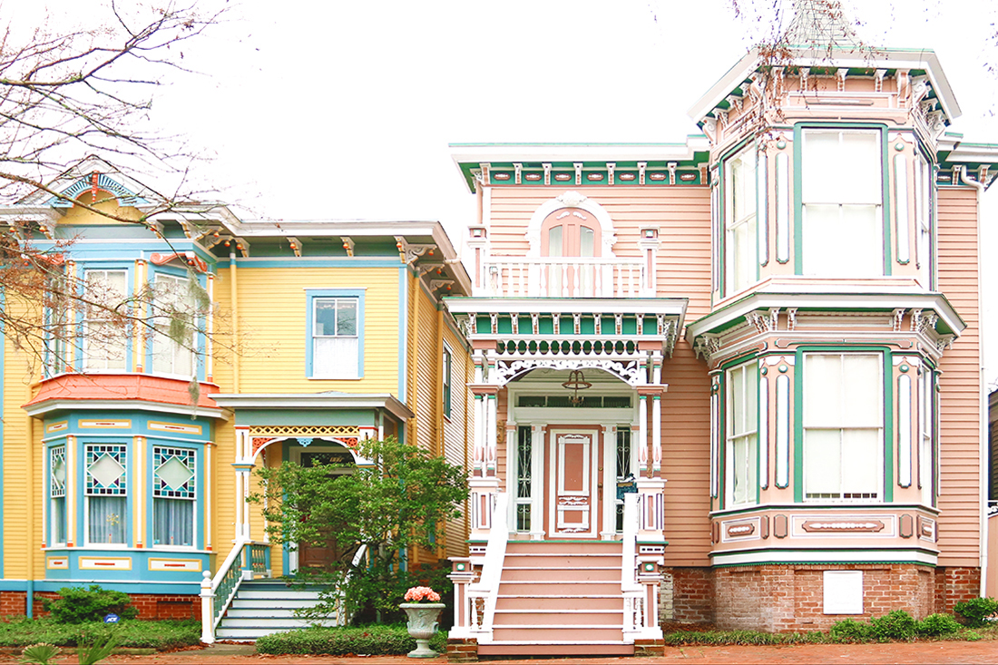A home in Savannah's Victorian District painted bright yellow with blue and orange trim is next to a traditional pink Victorian-style home with green and white trim.