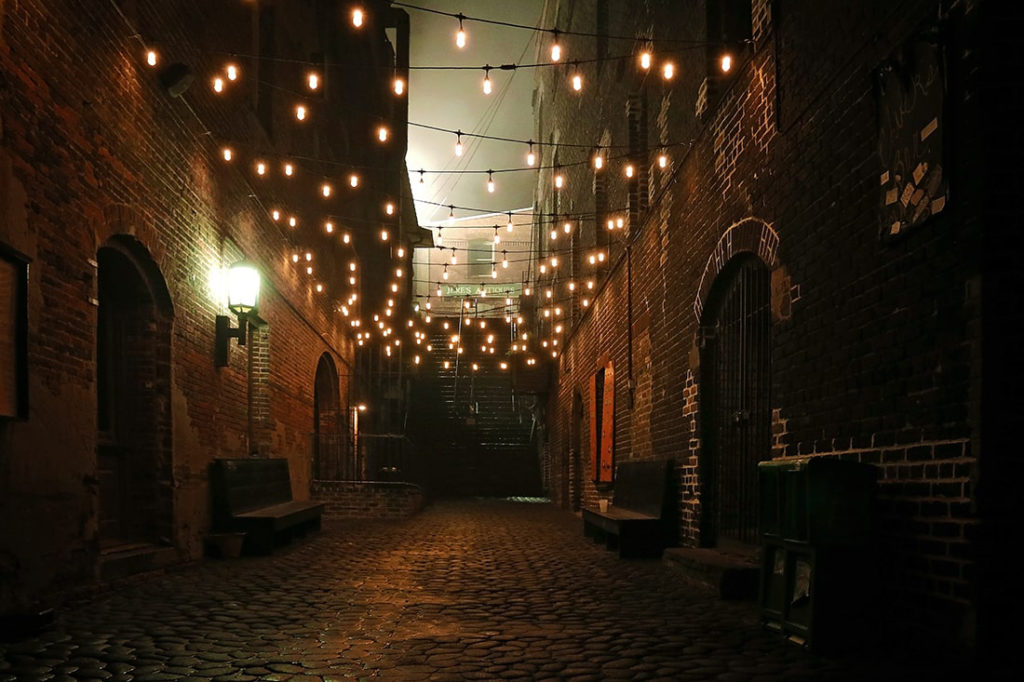 Dimly lit alleyway on River Street in Savannah with a cobblestone path leading to steep old stairs and a layer of mist covering the entire scene.