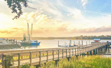 Hilton Head Island's Dockside Restaurant's long wooden pier with shrimp boats and a beautiful yellow sunset in the background.