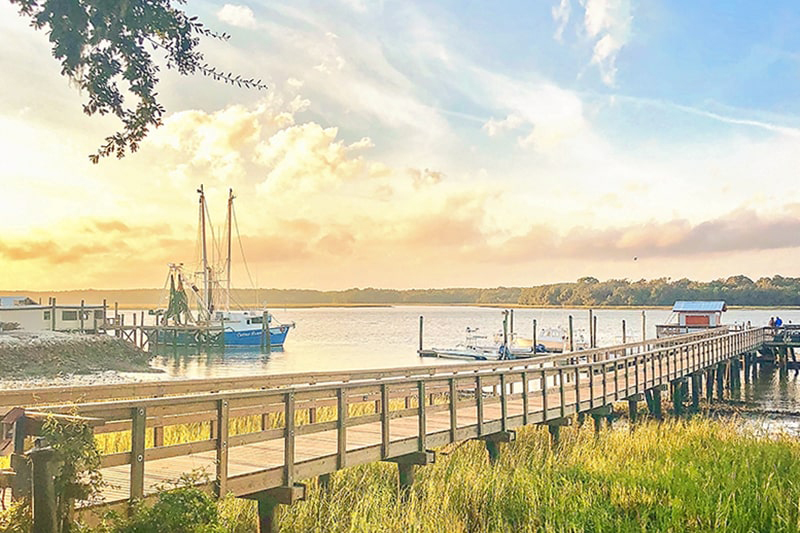 Hilton Head Island's Dockside Restaurant's long wooden pier with shrimp boats and a beautiful yellow sunset in the background.