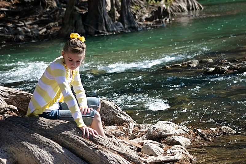 Cute pre-teen girl sitting at the edge of the Guadalupe River.