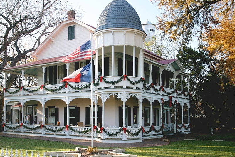 Gruene Mansion Inn exterior with Christmas decor draped on its wraparound porch.