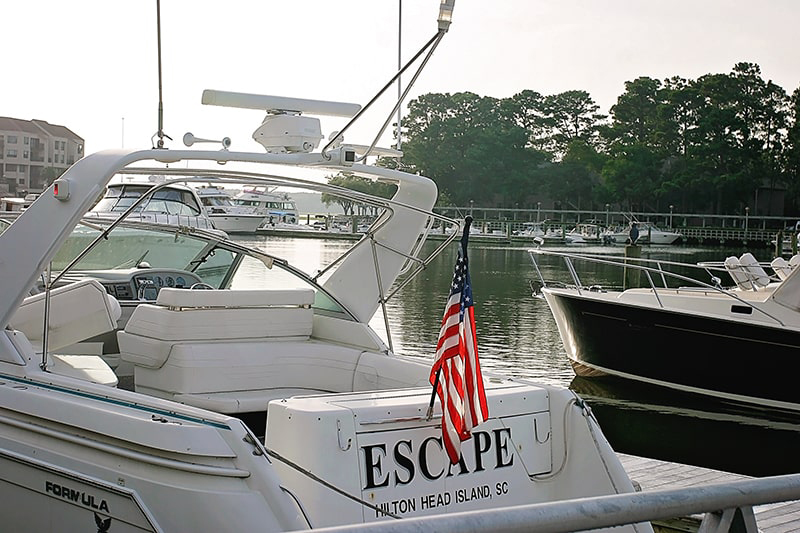 A yacht named Escape docked in Shelter Cove Harbour with an American flag on display.